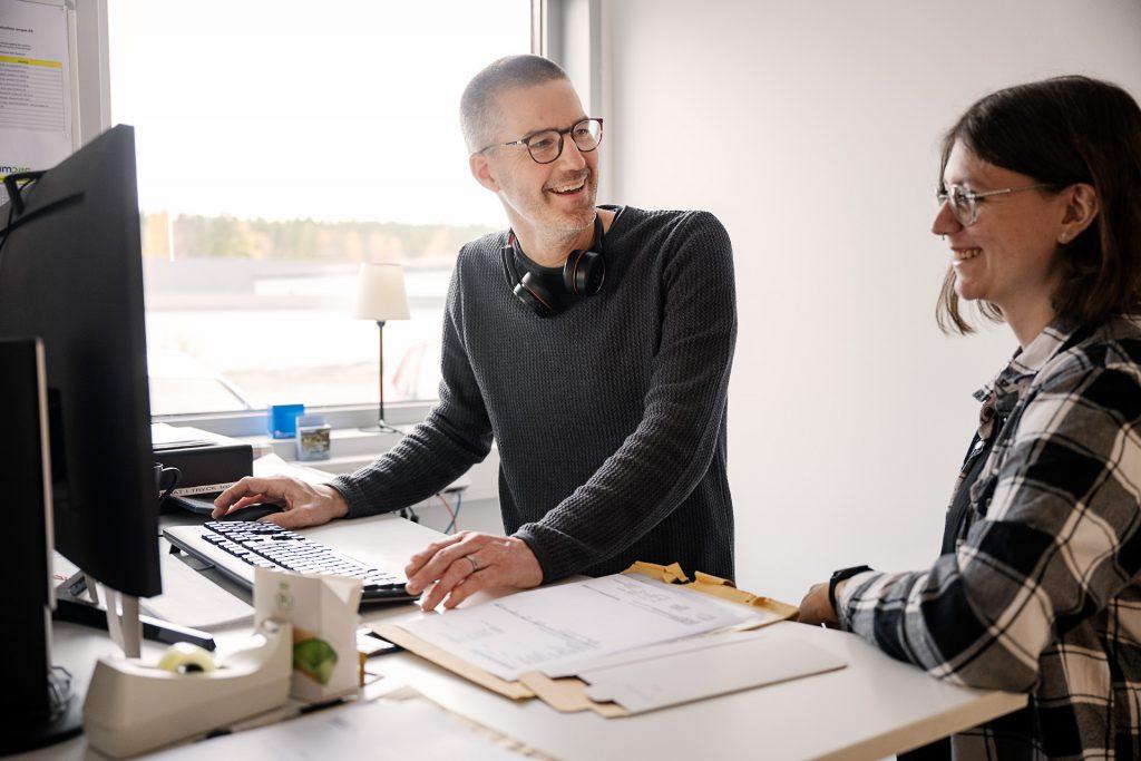 Två personer arbetar vid en dator och ser glada ut